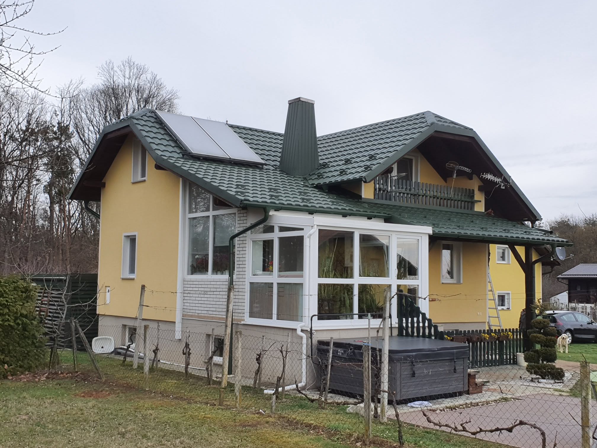 Zelena kovinska kritina z obrobljenim dimnikom in sončnimi kolektorji na družinski hiši