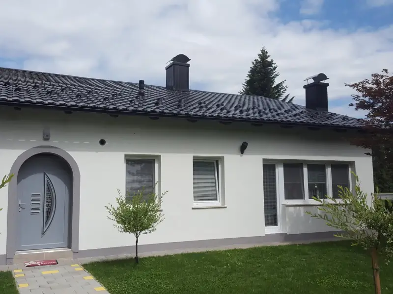 Antracitna kovinska kritina s snegobrani in obrobljenima dimnikoma na pritlični hiši